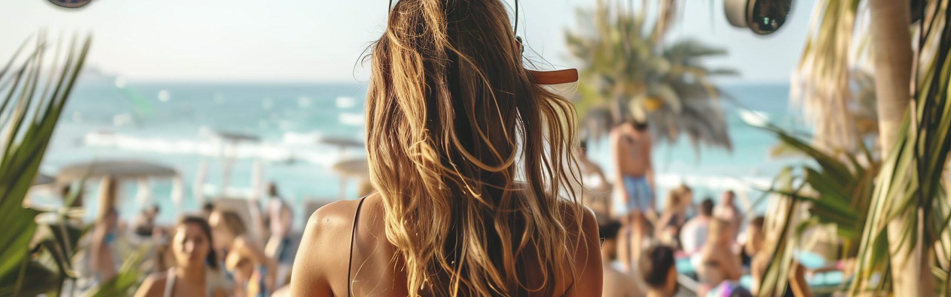 back view of beautiful woman DJ with headphones on stage at beach club, people dancing in background